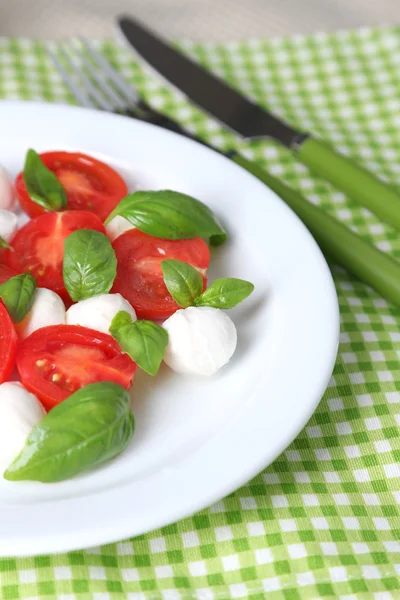 Sałatka Caprese z serem mozarella, pomidory i bazylia na talerzu, drewniany stół tło — Zdjęcie stockowe