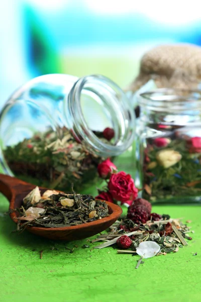 Surtido de hierbas y té en frascos de vidrio sobre mesa de madera, sobre fondo brillante — Foto de Stock