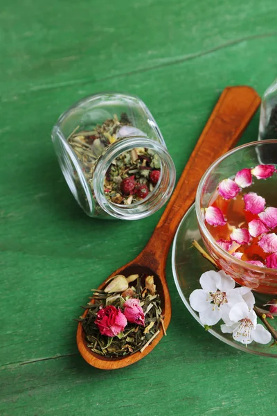 Assortimento di erbe aromatiche, tè in barattoli di vetro e tazza di bevanda calda su sfondo di legno — Foto Stock