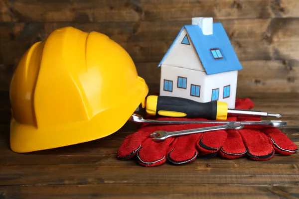 Composition avec casque de sécurité, gants en cuir, outils et maison décorative sur fond en bois — Photo