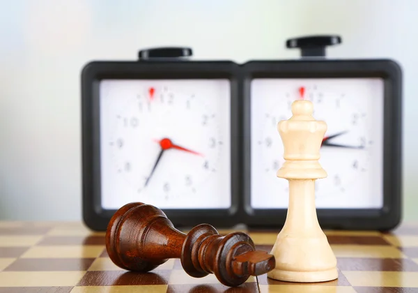 Tablero de ajedrez con ajedrez y reloj sobre fondo claro — Foto de Stock