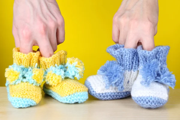 Hands with crocheted booties for baby, on color background — Stock Photo, Image