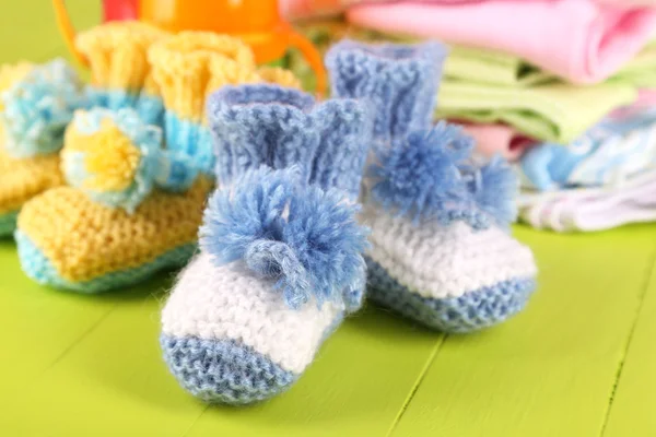 Composition with crocheted booties for baby,clothes, bottles on wooden background — Stock Photo, Image