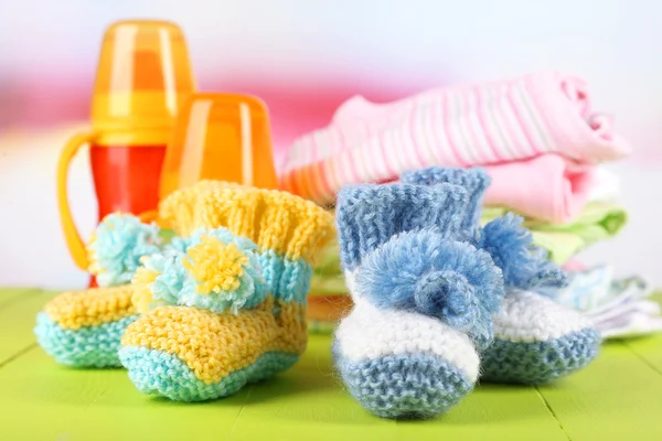 Composition with crocheted booties for baby,clothes, bottles on wooden background — Stock Photo, Image