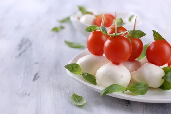 Smakelijke mozzarella kaas met basilicum en tomaten op plaat, op houten tafel — Stockfoto