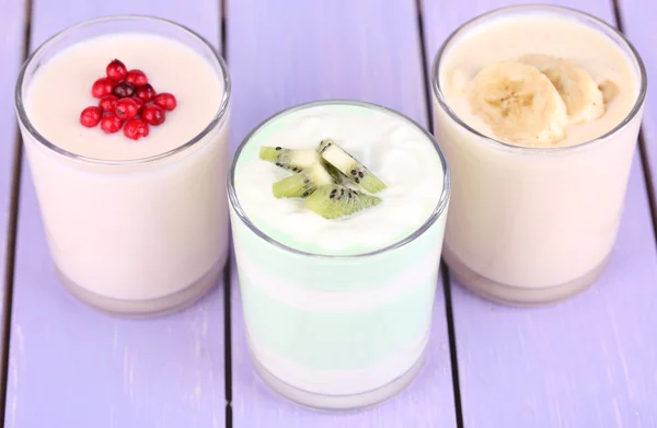 Delizioso yogurt con gusti di frutta in bicchieri e frutta fresca su sfondo di legno a colori — Foto Stock