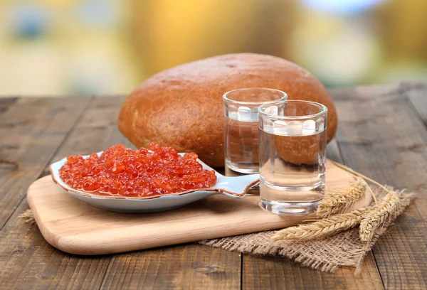 Composición con vasos de pan de vodka y caviar rojo sobre mesa de madera, sobre fondo brillante —  Fotos de Stock