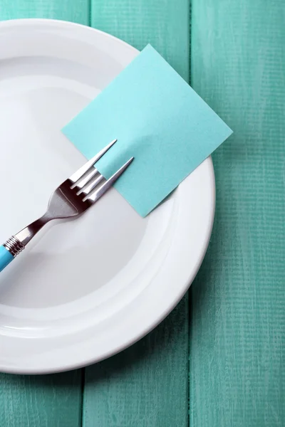 Empty note paper attached to fork, on plate, on color wooden background — Stock Photo, Image