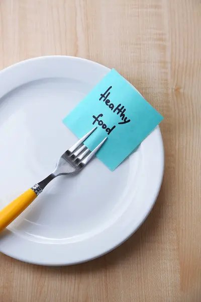 Note paper with message  attached to fork, on plate, on color wooden background — Stock Photo, Image