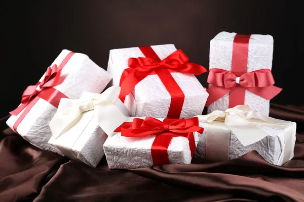 Hermosos regalos con cintas rojas sobre seda, sobre fondo oscuro —  Fotos de Stock