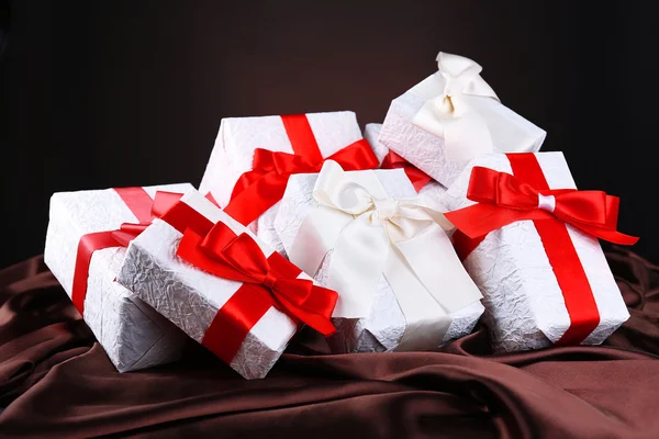 Schöne Geschenke mit roten Bändern auf Seide, auf dunklem Hintergrund — Stockfoto