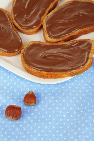 Brot mit süßem Schokoladen-Haselnussaufstrich auf Teller auf Tischdecke — Stockfoto