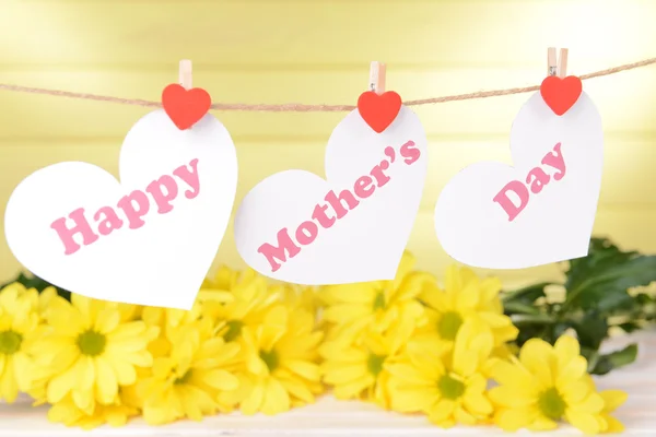 Happy Mothers Day message written on paper hearts with flowers on yellow background — Stock Photo, Image