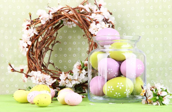 Composición con huevos de Pascua en frasco de vidrio y corona decorativa con ramas florecientes sobre fondo claro —  Fotos de Stock