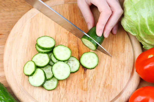 Frauenhände schneiden Gurken auf Holzbrett, Nahaufnahme, auf Holzgrund — Stockfoto