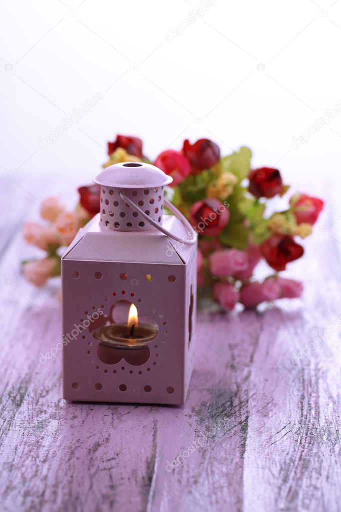 Decorative metallic lantern and artificial flowers on color wooden table, on light background