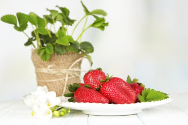 çilek plaka üzerinde açık renkli ahşap masa üzerinde yaprakları ile