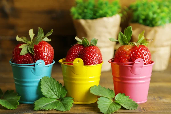 Strawberries with in decorative buckets on wooden background — Stock Photo, Image