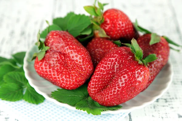 Strawberries with leaves on plate, on wooden background — Stock Photo, Image