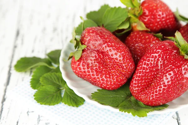 Erdbeeren mit Blättern auf Teller, auf Holzgrund — Stockfoto