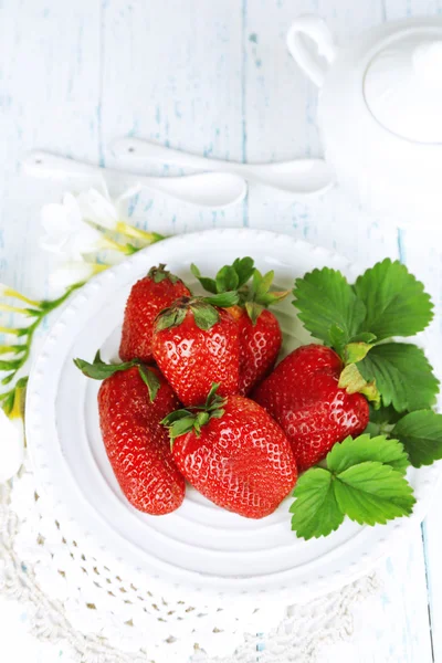 Fresas con hojas en plato, sobre fondo de madera — Foto de Stock