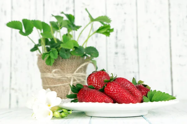 Strawberries with leaves on plate, on wooden background — Stock Photo, Image