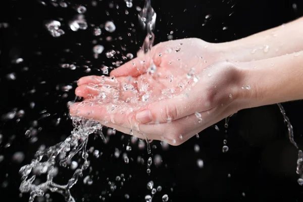 Manos humanas con agua salpicando sobre ellas sobre fondo negro — Foto de Stock