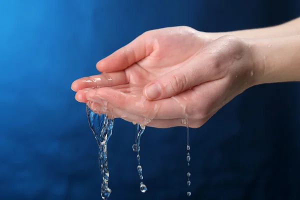 Menschliche Hand mit Wasser, das auf sie spritzt, auf dunkelblauem Hintergrund — Stockfoto