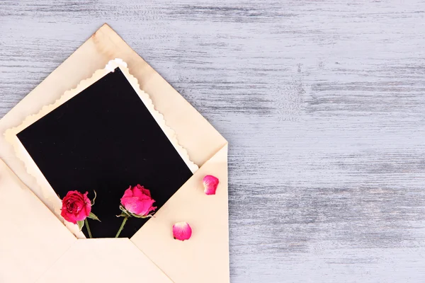 Envelope velho com papel fotográfico em branco e belas rosas rosa secas em fundo de madeira — Fotografia de Stock