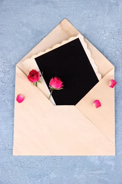Старий конверт з чистим фотопапером і красивими рожевими сушеними трояндами на дерев'яному фоні — стокове фото