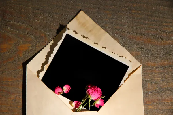 Vecchia busta con carta fotografica vuota e belle rose rosa secche su sfondo di legno — Foto Stock