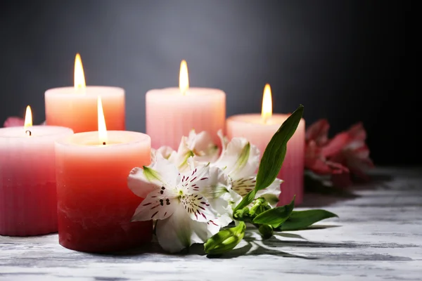 Vackert ljus med blommor på träbord, på mörk bakgrund — Stockfoto