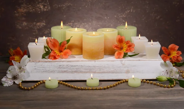 Mooie kaarsen met bloemen op tafel op bruine achtergrond — Stockfoto