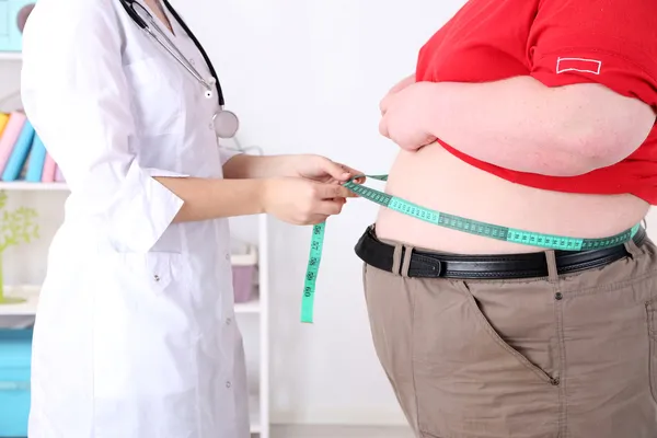 Arzt untersucht Fettleibigkeit bei Patienten vor hellem Hintergrund — Stockfoto