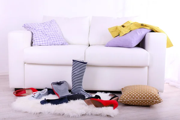 Chaotisch bunte Kleidung und Schuhe auf Sofa auf hellem Hintergrund — Stockfoto