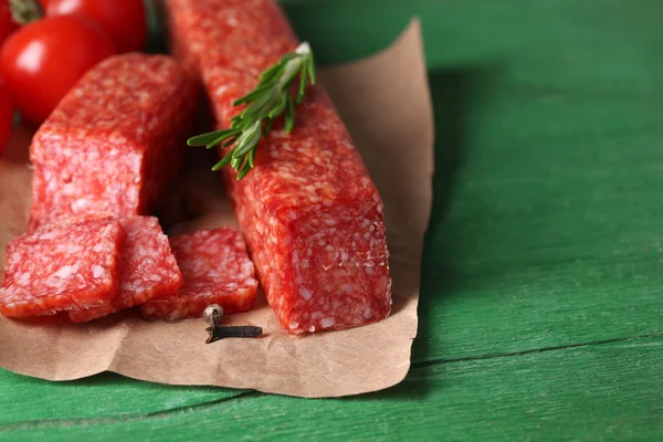 Tasty salami sausage, vegetables and spices on paper wooden background — Stock Photo, Image