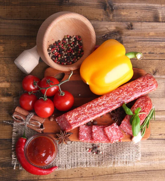 Smakelijke salami worst en specerijen op houten achtergrond — Stockfoto