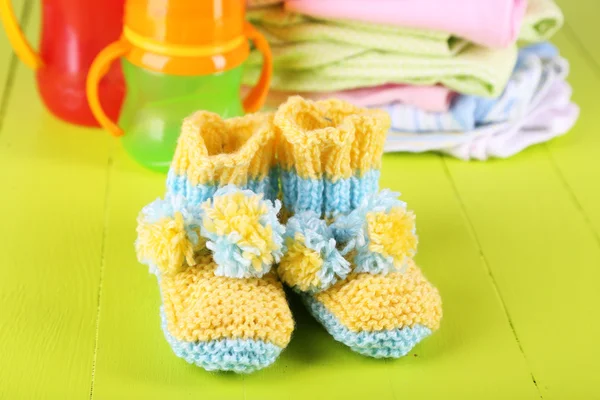 Composition with crocheted booties for baby,clothes, bottles on wooden background — Stock Photo, Image