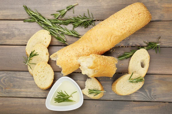 Fresh bread with olive oil and rosemary on wooden table — Stock Photo, Image