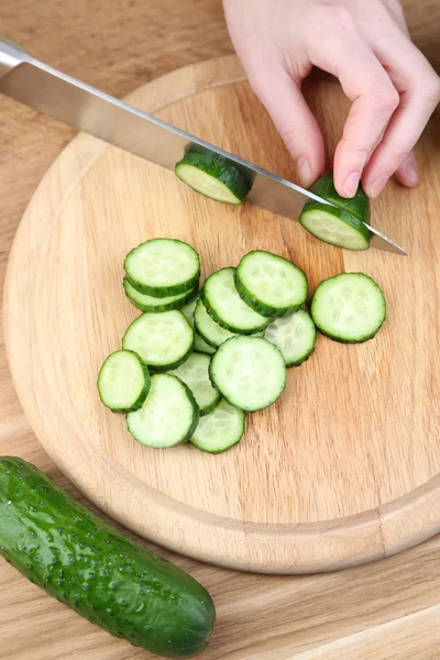 Female hands cutting cucumber on wooden board, close-up, on wooden background — Stock Photo, Image