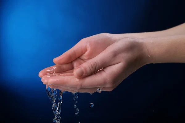 Main humaine avec éclaboussures d'eau sur eux sur fond bleu foncé — Photo