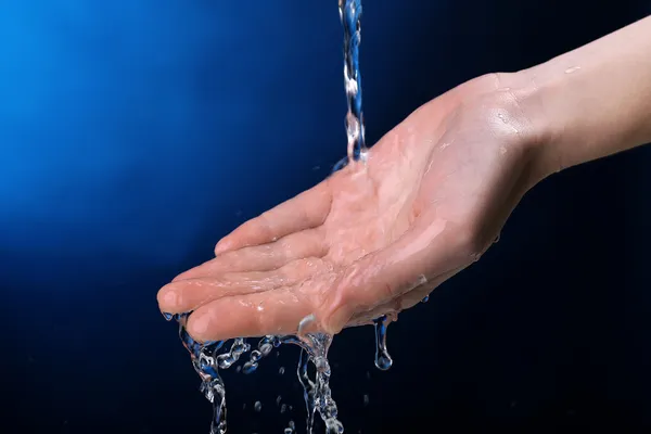 Menschliche Hand mit Wasser, das auf sie spritzt, auf dunkelblauem Hintergrund — Stockfoto