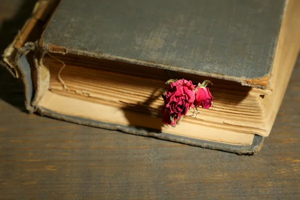 Old book with beautiful pink dried roses on old wooden background — Stock Photo, Image