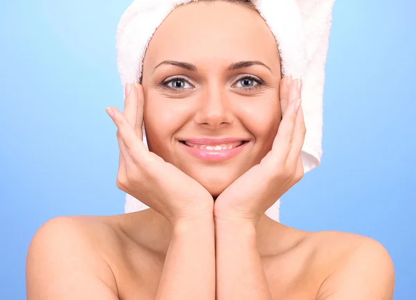 Beautiful young woman after shower with a towel on her head on blue background close-up — Stock Photo, Image