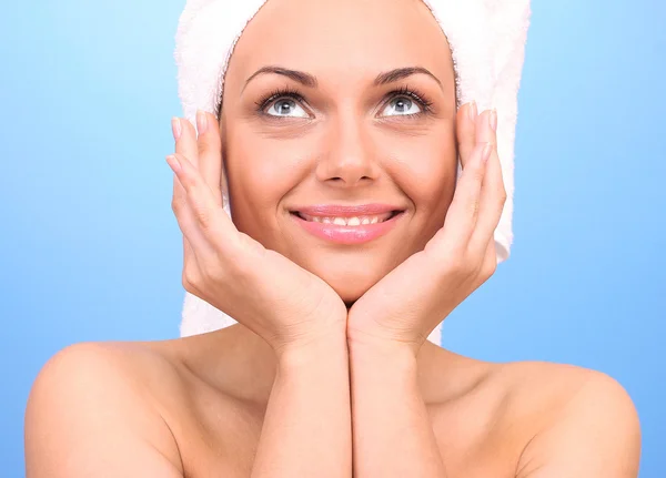 Beautiful young woman after shower with a towel on her head on blue background close-up — Stock Photo, Image