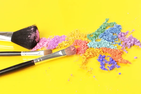Crushed eyeshadow and professional make-up brush on yellow background — Stock Photo, Image