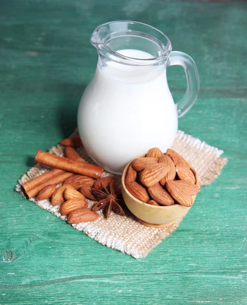 Almond milk in jug with almonds in bowl, on color wooden background — Stock Photo, Image
