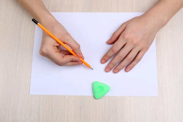 Mänskliga händer med penna skriva på papper och radera gummi på träbord bakgrund — Stockfoto
