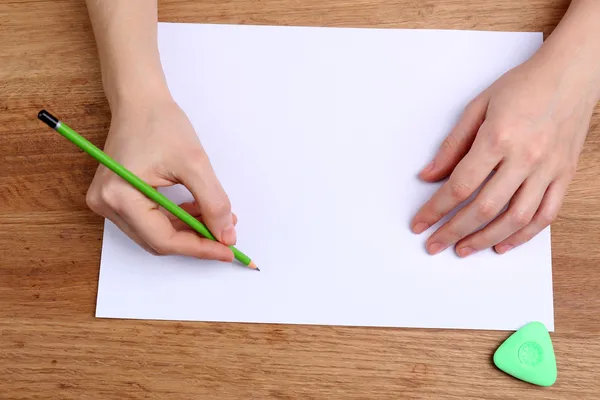 Mani umane con scrittura a matita su carta e cancellare gomma su sfondo tavolo di legno — Foto Stock