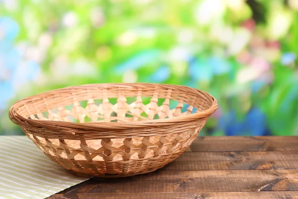 Panier en osier vide sur table en bois, sur fond lumineux — Photo